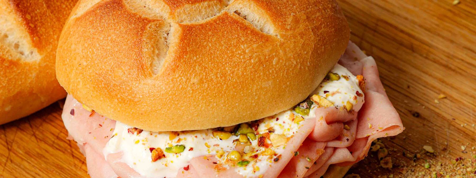 Il Panino di Willie – Mortadella-Panino mit Stracciatella und Pistazien auf einem Holzbrett